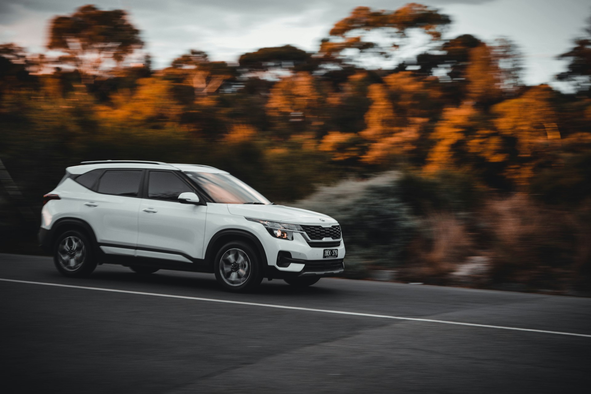 a white suv driving down a road next to a forest